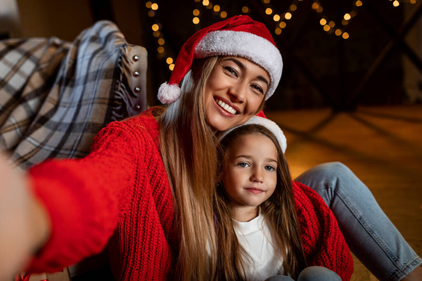 Ποβ ευτυχισμένης γυναίκας και κόρης να μιλάνε σέλφι τα Χριστούγεννα. - Φωτογραφία, εικόνα
