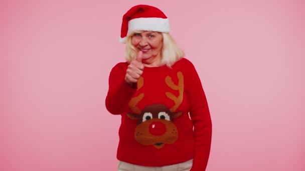 Nagymama piros újévi pulóvert visel szarvasokkal, felemeli a hüvelykujját, és egyetért valami jóval, mint például: - Felvétel, videó