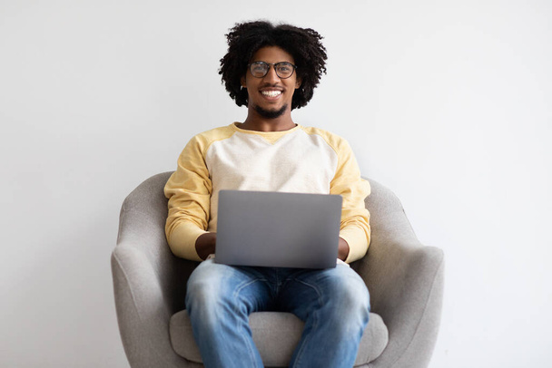 Etätyö. Onnellinen nuori musta freelancer kaveri istuu kannettavan nojatuolissa - Valokuva, kuva