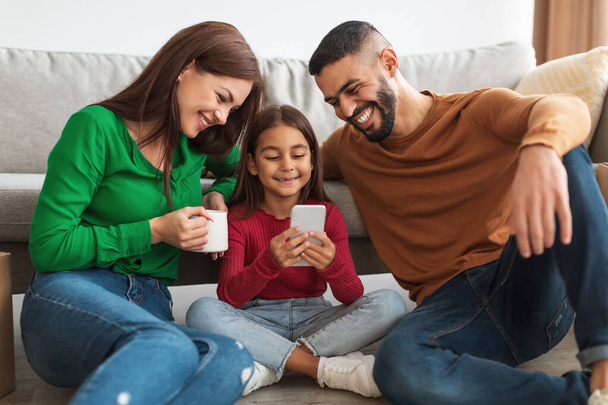 Happy Arab family of three people holding and using smartphone - Fotoğraf, Görsel