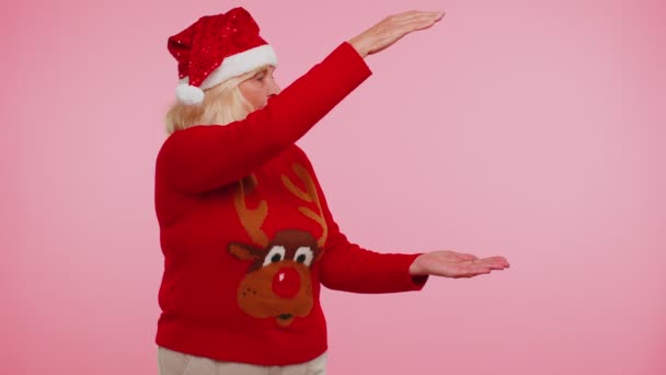 Grandmother in Christmas deer sweater showing thumbs up and pointing at on blank advertisement space - Footage, Video