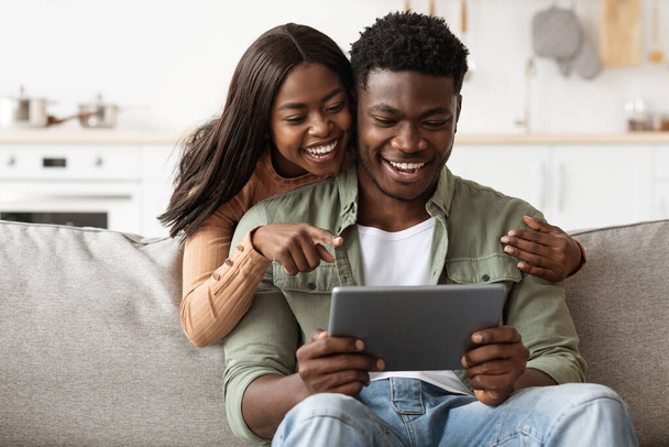 Веселая африканская американская пара развлекается дома, используя блокнот - Фото, изображение
