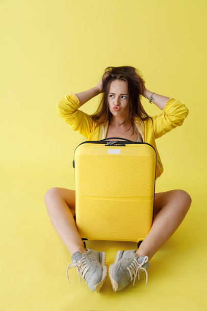 Γοητευτική γυναίκα με ταξιδιωτική τσάντα κάθεται στο στούντιο - Φωτογραφία, εικόνα