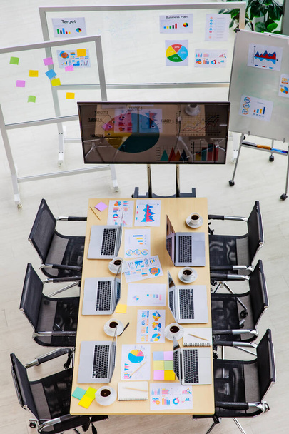 Vista superior de la sala de reuniones de la conferencia en la oficina de la empresa llena de computadoras portátiles portátiles en el escritorio con sillas negras y monitor de pantalla grande y tablero de vidrio con documentos de papel de datos poste. - Foto, imagen