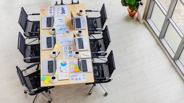 Снимок конференц-зала в офисе компании, заполненного ноутбуками на рабочем столе с черными стульями и большим экраном монитора и стеклянной доской с вывеской бумажных документов. - Фото, изображение