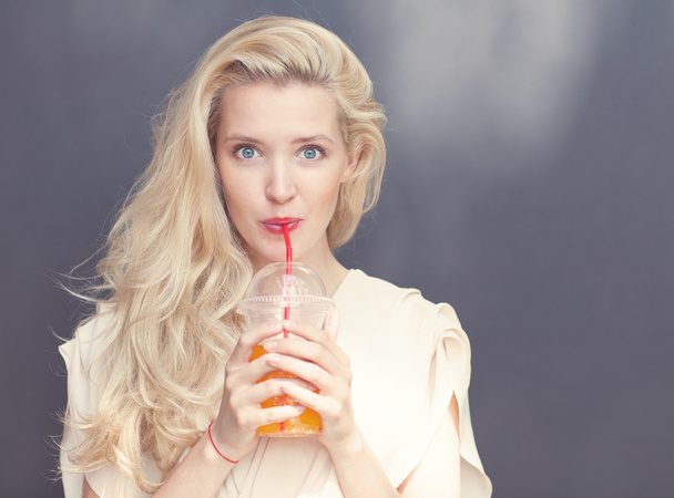 Beautiful sexy blonde with blue eyes drinking beverage through a straw on a hot summer day near the wall. Toned in warm colors - Foto, Bild