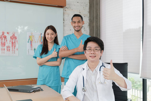 Treuhandteam des Gesundheitswesens, Porträt von drei jungen Ärzten asiatischer Herkunft in Uniform mit Stethoskop, lächelnd und in die Kamera blickend in der Klinik, Personen, die sich mit professioneller Behandlung auskennen. - Foto, Bild