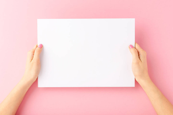 Woman hands showing white paper with copyspace on pink background. Close up - Photo, Image
