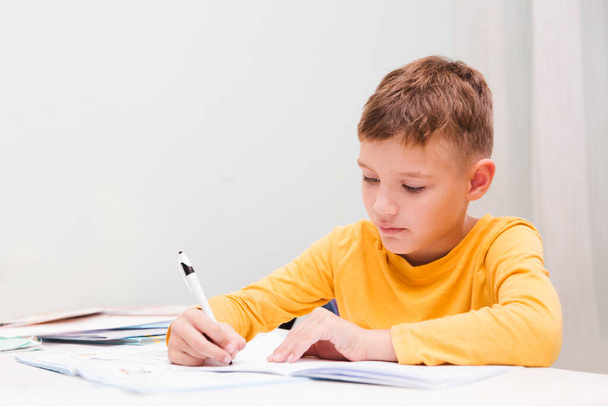 schoolboy do lessons and writes tasks to notebooks at home. homeschooling, distant learningstudy online at home.  - Valokuva, kuva