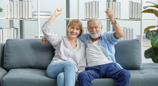 Kaukasische alte Senioren Großelternpaar in lässiger Kleidung grauen Bart und Haare Ehemann und Oma Frau sitzen schreiend lächelnd jubelnd Sport Sieg mit aufgeregter Aktion gewinnen. - Foto, Bild