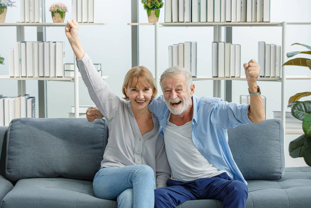 Καυκάσιος ηλικιωμένοι παππούδες ζευγάρι σε casual φορούν γκρι γενειάδα και μαλλιά σύζυγος και η γυναίκα γιαγιά κάθεται φωνάζοντας χαμογελώντας ικανοποιώντας επευφημίες αθλητισμού νίκη με ενθουσιασμένοι δράση. - Φωτογραφία, εικόνα