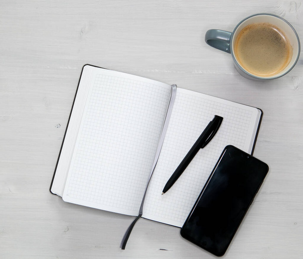 otevřený bílý notebook, černý mobilní telefon a šálek kávy na světle dřevěném pozadí - Fotografie, Obrázek