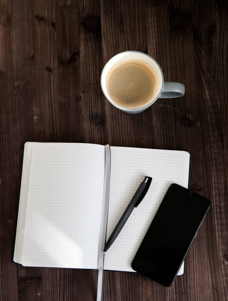 caderno branco aberto, um telefone celular preto e uma xícara de café em um fundo de madeira escura - Foto, Imagem