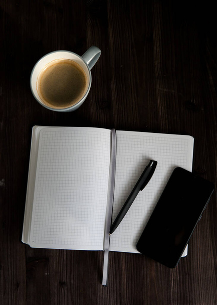 otwarty biały notatnik, czarny telefon komórkowy i filiżanka kawy na ciemnym drewnianym tle - Zdjęcie, obraz