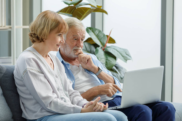 Close up shot of Caucasian old senior elderly grandparents lover couple sitting together on couch in living room look at laptop computer screen learning internet social network online on website. - Photo, Image
