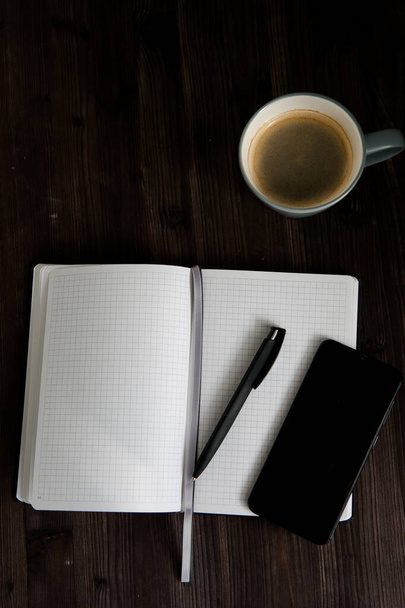 открыть белый ноутбук, черный мобильный телефон и чашку кофе на темном деревянном фоне - Фото, изображение