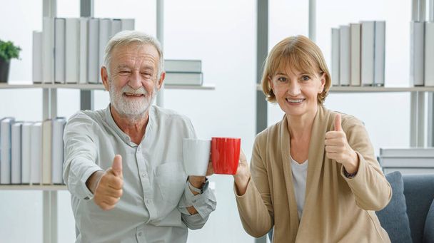 Caucasian old senior happy lovely couple grandparent gray bearded husband and pretty wife relaxing drinking hot coffee cups together. - Photo, Image