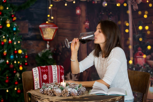 Middle aged woman, drinking red wine at home, cozy christmas atmosphere in a wooden cottage - Photo, image