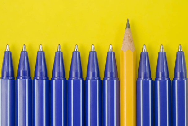 Bolígrafos azules y un lápiz amarillo sobre fondo amarillo. Concepto de individualidad. - Foto, Imagen