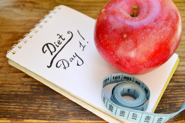 Ernährungskonzept mit rotem Apfel, Notizbuch und blauem Maßband auf Holztisch - Foto, Bild