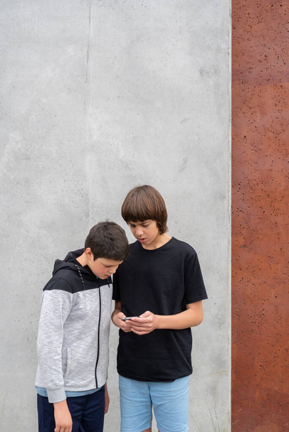 Двоє підлітків дивляться на мобільний телефон, стоячи перед бетонною стіною в міському парку з копіюванням космічного апарата - Фото, зображення