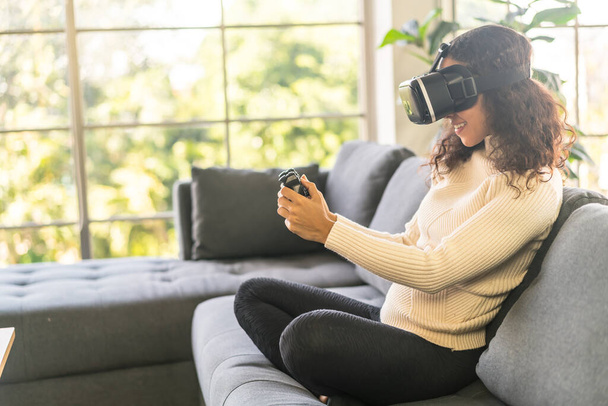 Latin woman using a virtual reality headset on sofa at home - Foto, imagen