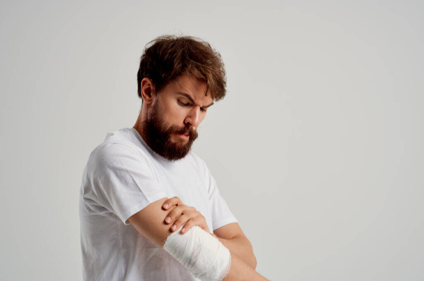 male patient in a white T-shirt with a bandaged hand  on light background. High quality photo - Foto, Imagen