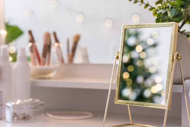 Reflection of christmas tree, light bulbs, in table mirror on woman dressing table with make up accessories - Fotoğraf, Görsel