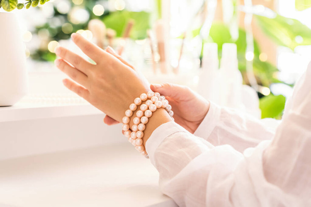Woman puts on jewelry, pearl bracelets on the hand and  sitting near dressing table with make up accessories. - Foto, Bild
