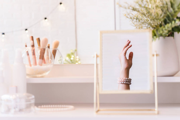 Christmas, light bulbs, eucalyptus, fir,  pine branches in a vase on dressing table with make up accessories. Reflection in table mirror of woman hand in pearl bracelets - Photo, Image