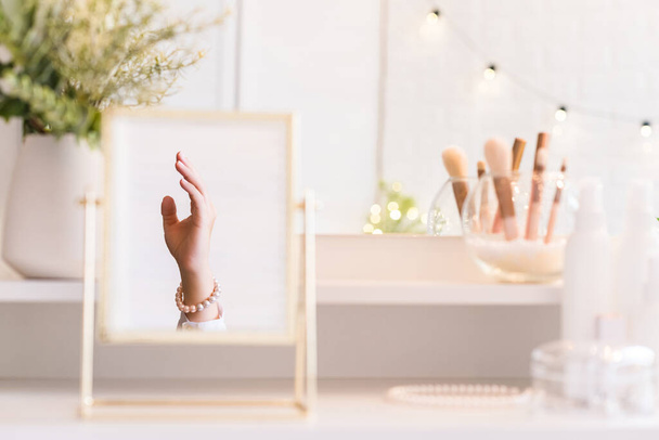 Reflection in table mirror of woman hand  in pearl bracelets on dressing table with make up accessories. Self-Care.  - Photo, Image