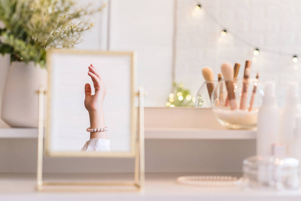 Christmas, light bulbs, eucalyptus, fir,  pine branches in a vase on dressing table with make up accessories. Reflection in table mirror of woman hand in pearl bracelets - Valokuva, kuva