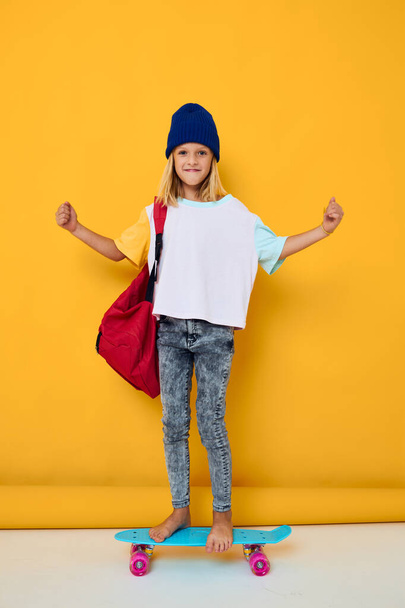 portrait of a girl rides a skateboard with a red backpack yellow background - Photo, Image