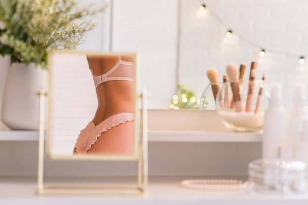 Reflection in table mirror of woman in underwear on dressing table with make up accessories. Self-Care.  - Φωτογραφία, εικόνα