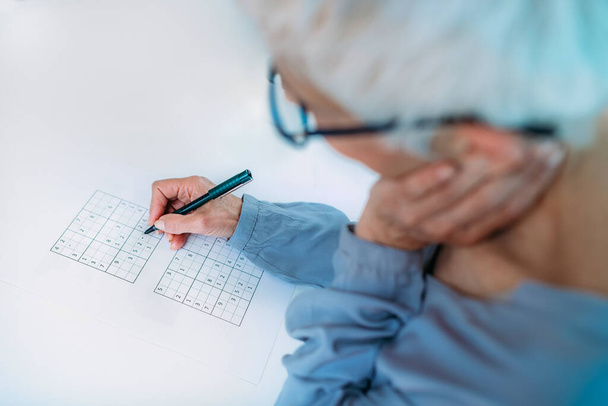 Kognitív tréning. Idősebb nő sudoku rejtvényeket old meg. - Fotó, kép