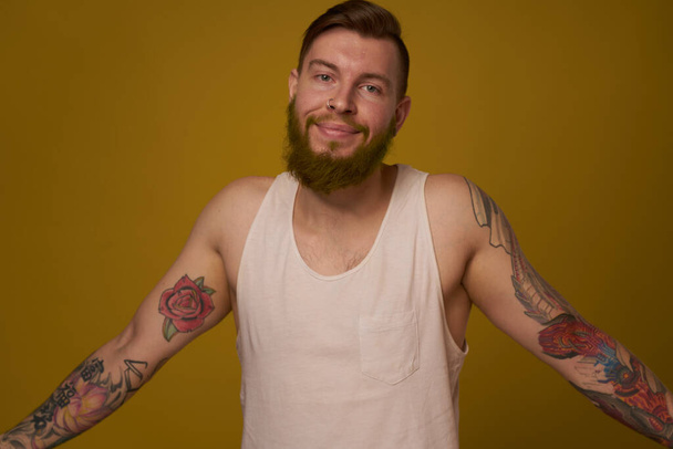 Cheerful bearded man in a white T-shirt with hooligan tattoos on his arms - Fotó, kép