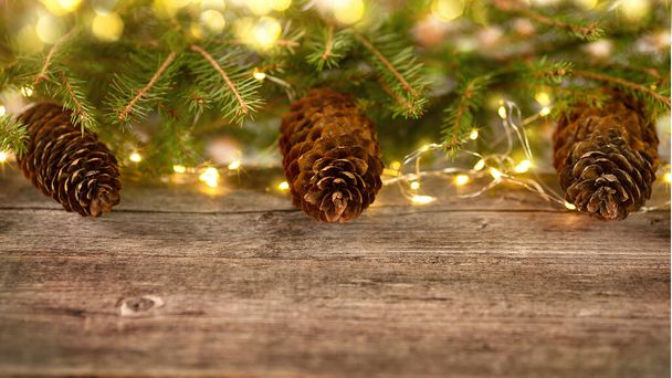 Branches of a Christmas tree with big cones on an old wooden table with lights from a garland in the background. Copy space - Foto, Imagem