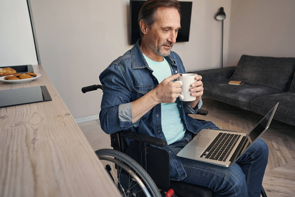Gelukkige man met een handicap drinken koffie met laptop - Foto, afbeelding
