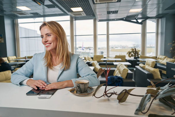 High-spirited female traveler sitting in airport cafe - Foto, afbeelding