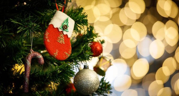 Detailní záběr červené a bílé vánoční dekor ponožka visí zdobení na zelené vánoční borovice větev s lesklé hůl koule koule a zvonek v přední rozmazané zlaté nízké světlo bokeh pozadí. - Fotografie, Obrázek