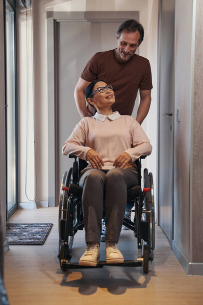Догляд за людиною, яка допомагає усміхненій жінці з інвалідністю в приміщенні
 - Фото, зображення