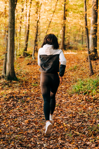 Girl jogging thru the forest in the fall season. Fitness outdoors concept. - Foto, afbeelding