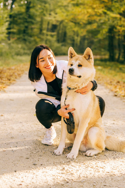 Portrait d'une fille heureuse promenant son chien de compagnie dans la forêt pendant l'automne. Vie de race Akita inu. - Photo, image