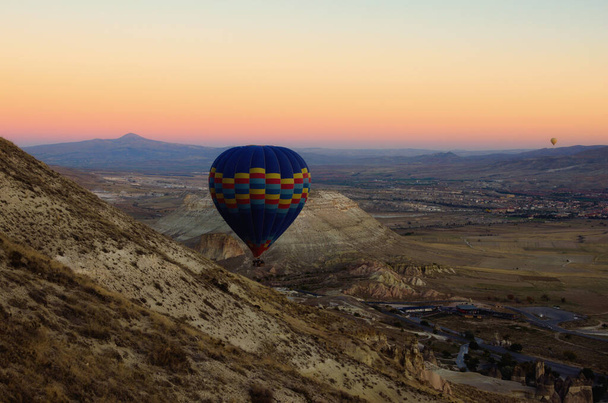Horkovzdušný balón letí blízko hory a skal. Scénický pohled na krajinu při východu slunce na neobvyklou skalní formaci v Cappadocii. Koncept cestování a cestovního ruchu. - Fotografie, Obrázek