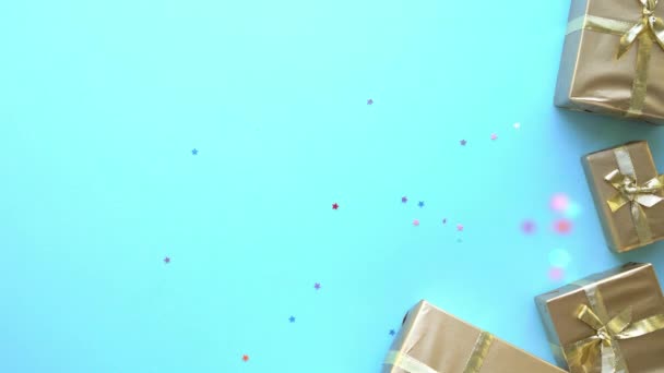destellos multicolores festivos en forma de estrellas caen sobre un fondo azul con regalos de oro - Metraje, vídeo