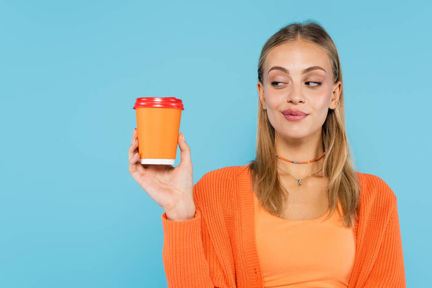 Young blonde woman looking at coffee to go isolated on blue  - Photo, image