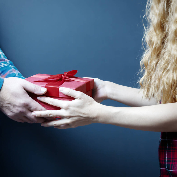Női és férfi kezek egy piros ajándékdobozt tartanak masnival. Egy ajándék két személyre. - Fotó, kép