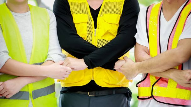 Επαγγελματική αγνώστων στοιχείων αρσενικό αρχιτέκτονα και μηχανικός επιστάτης συναδέλφους σε ανακλαστικά κίτρινα γιλέκα ασφαλείας στέκεται κρατώντας τα χέρια μαζί κάνουν συμφωνία ως ομαδική εργασία στο εργοτάξιο. - Φωτογραφία, εικόνα