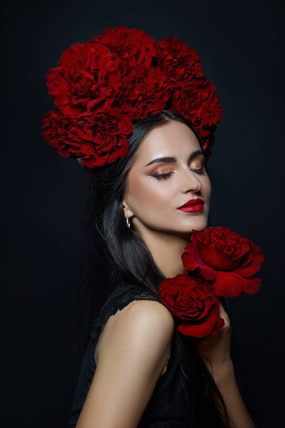 Beauty portrait brunette woman with crown of roses flowers on her head. Bright red makeup and lipstick. Rose flowers in the hands of a woman - Photo, Image