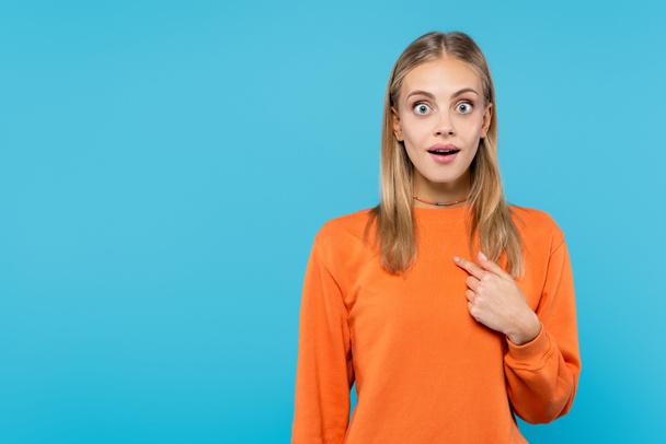 Shocked blonde woman pointing with finger isolated on blue  - Foto, immagini